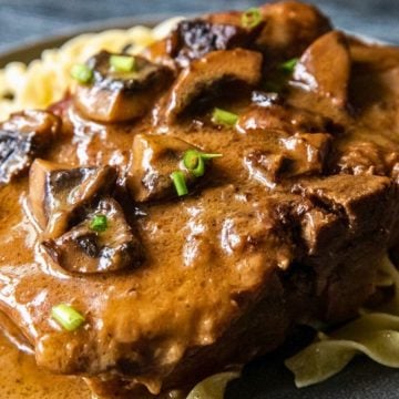 Beef steak with creamy mushroom sauce served over egg noodles, garnished with chopped green onions.