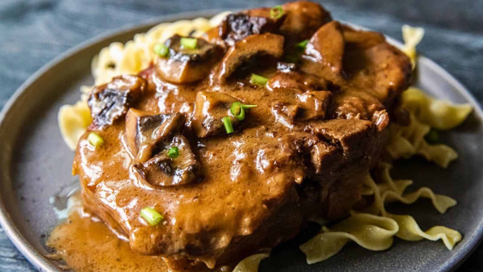 Beef steak with creamy mushroom sauce served over egg noodles, garnished with chopped green onions.