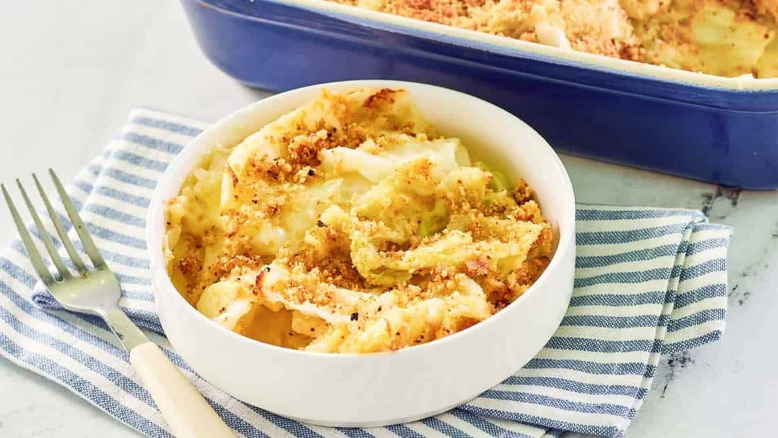 Bowl of baked macaroni and cheese with breadcrumbs on top, beside a fork and a casserole dish.