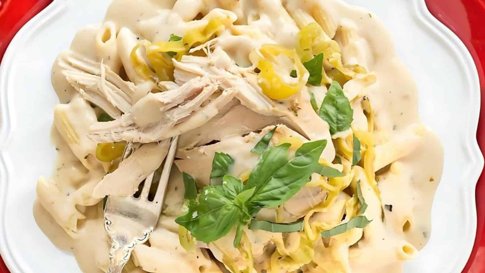 White plate of creamy pasta with shredded chicken, yellow peppers, and basil, with a fork.