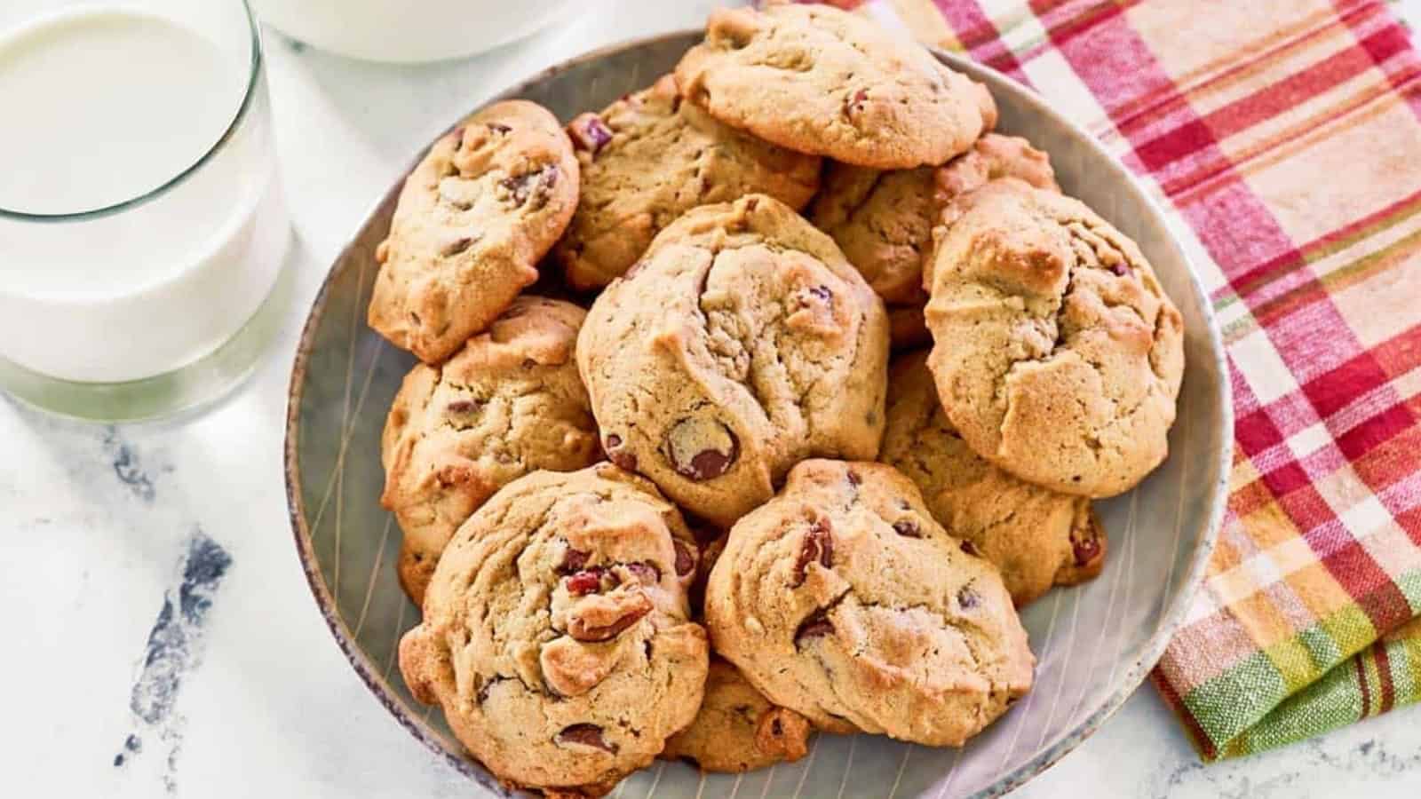 A plate of chocolate chip cookies next to two glasses of milk and a colorful plaid napkin.
