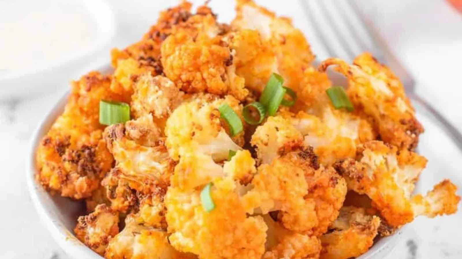 Close-up of crispy roasted cauliflower bites garnished with chopped green onions in a white bowl.