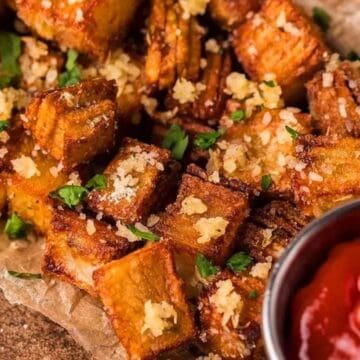 Crispy stacked potatoes topped with grated cheese and parsley beside a cup of ketchup.
