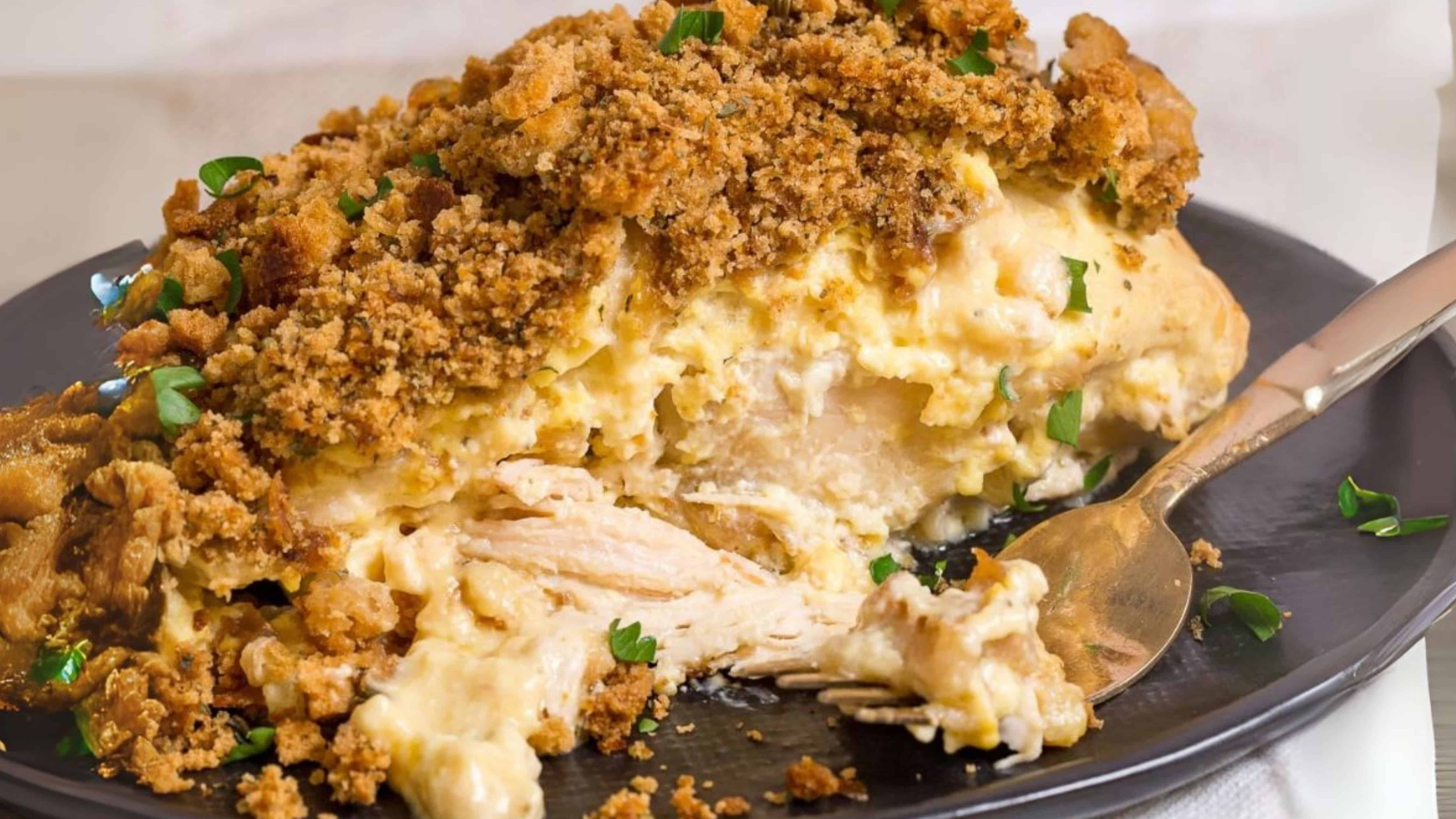 Creamy chicken casserole topped with golden brown breadcrumbs, served on a black plate with a spoon.
