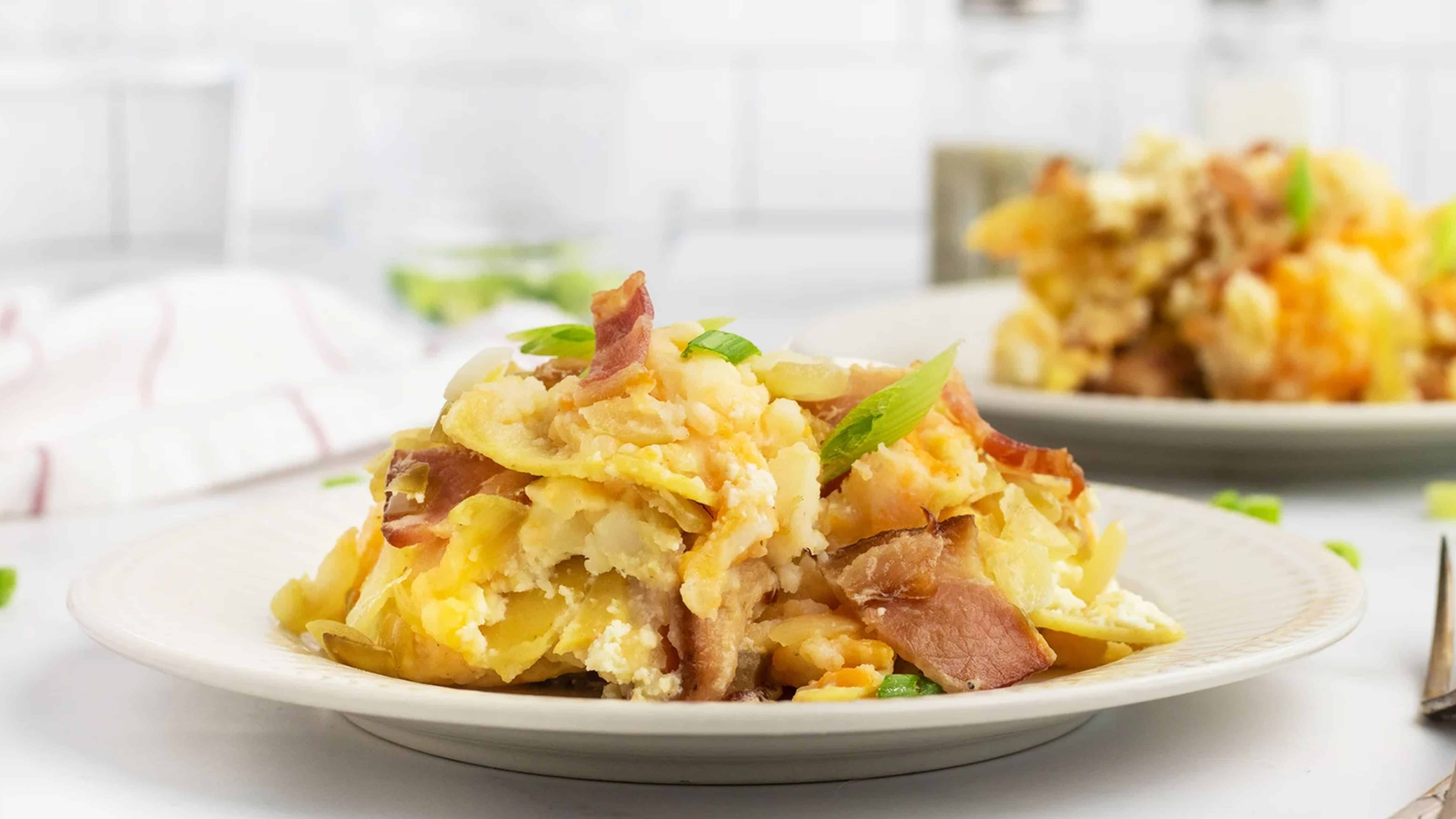 A serving of cheesy potato casserole with bacon and green onions on a white plate.