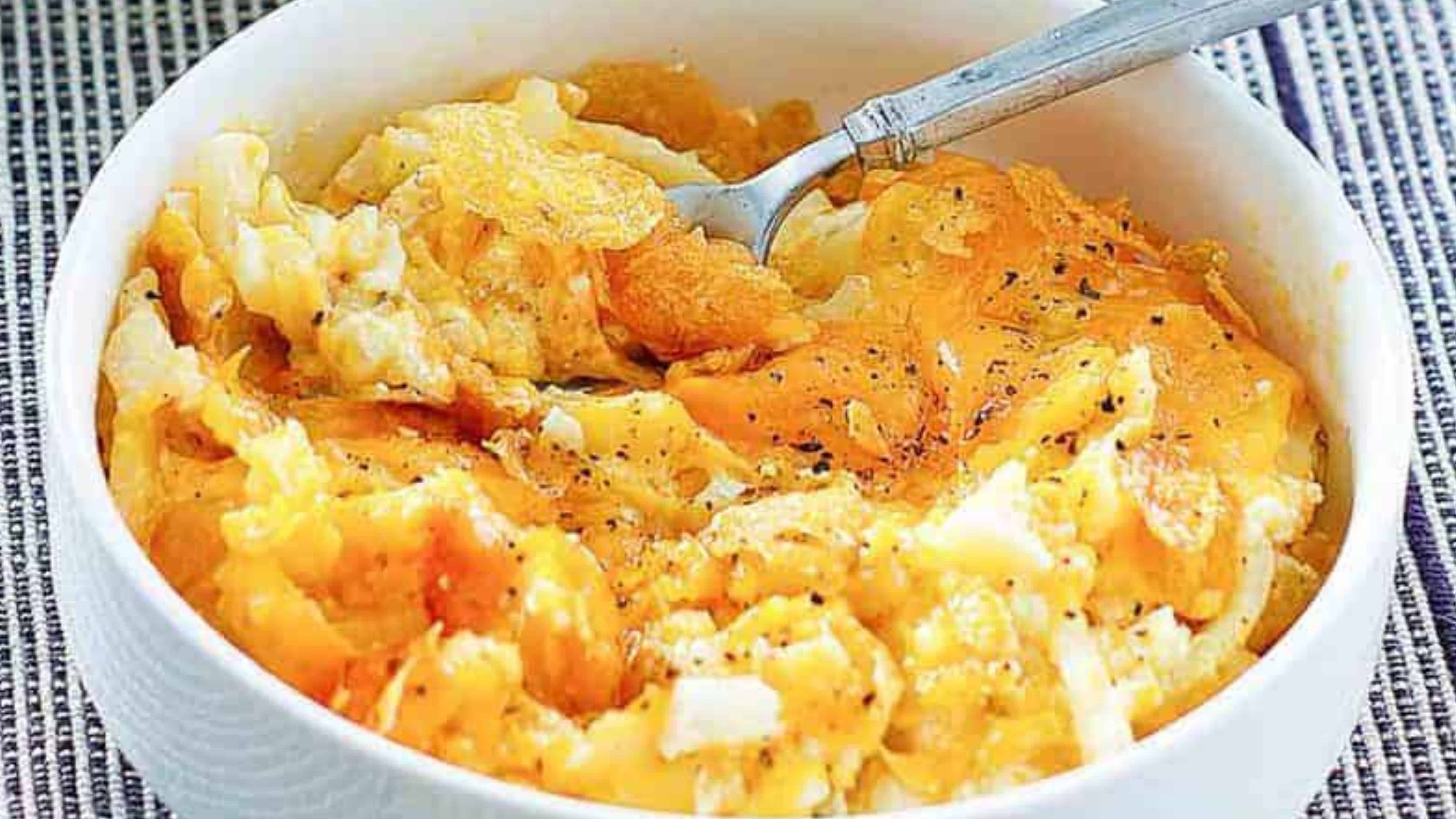 A bowl of cheesy hashbrown casserole topped with black pepper, with a fork inside.