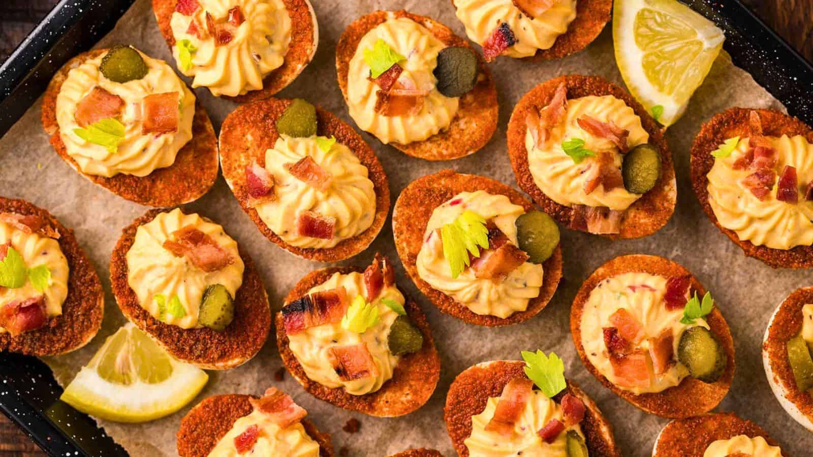 Deviled eggs served on crispy bases, topped with bacon, pickles, herbs, and garnished with lemon wedges.
