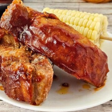 Barbecue pork ribs with sauce on a white plate, served with a skewer of corn on the cob.
