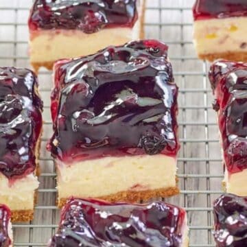 Nine blueberry cheesecake bars with a shiny berry topping are cooling on a wire rack.