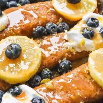 Three crepes topped with blueberries, lemon slices, whipped cream, and syrup on a plate.