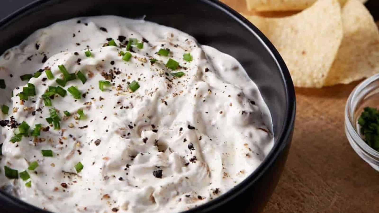 Creamy dip with herbs and cracked pepper in a black bowl, served with tortilla chips on the side.