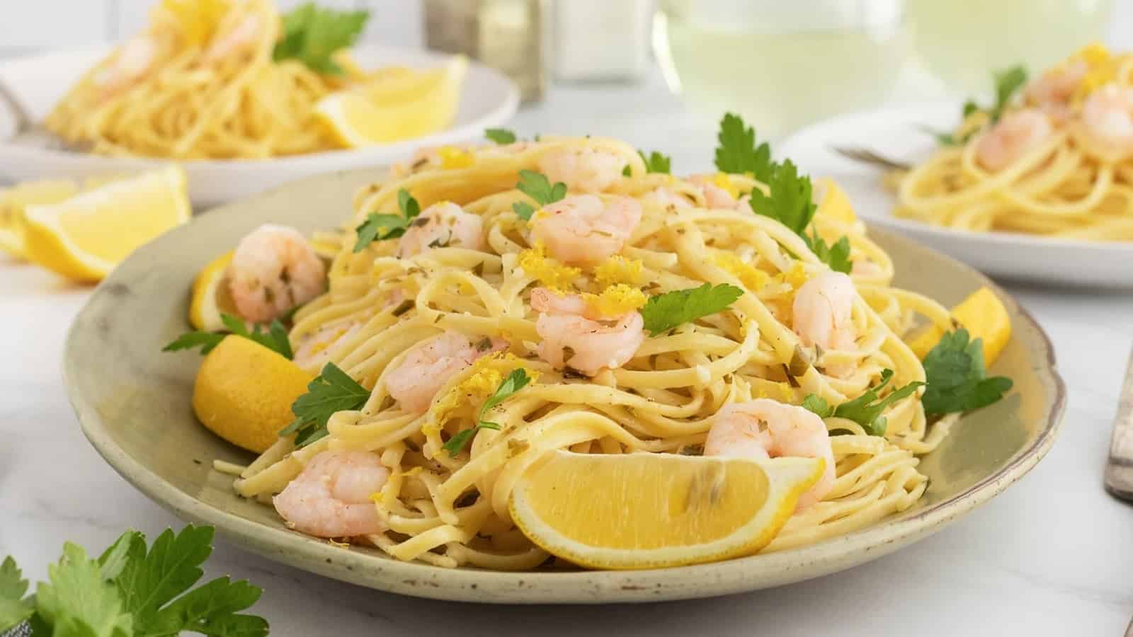 A plate of shrimp pasta garnished with lemon wedges and parsley, with more plates in the background.
