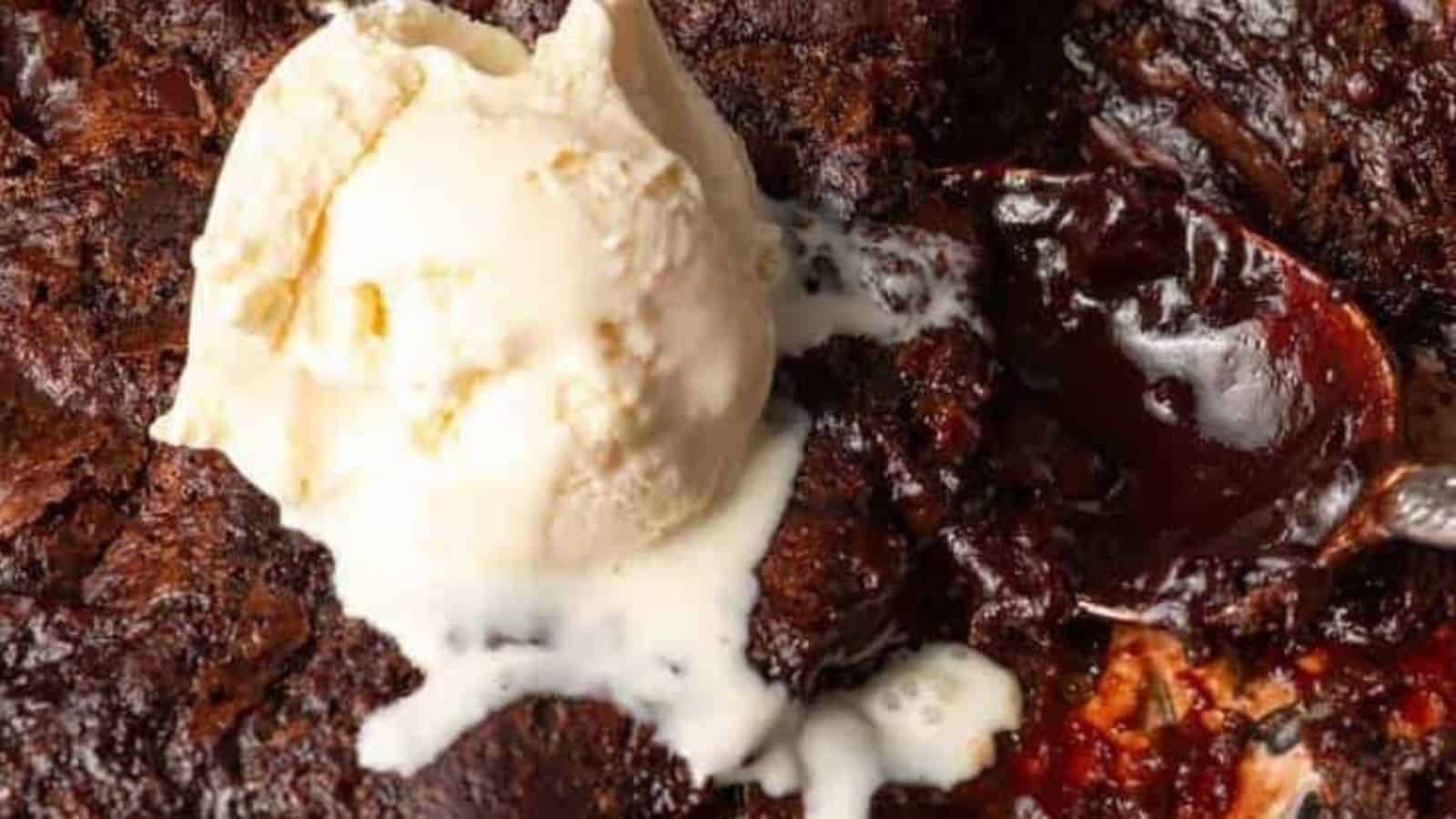 A scoop of vanilla ice cream melting on top of rich, gooey chocolate lava cake with a spoon beside it.