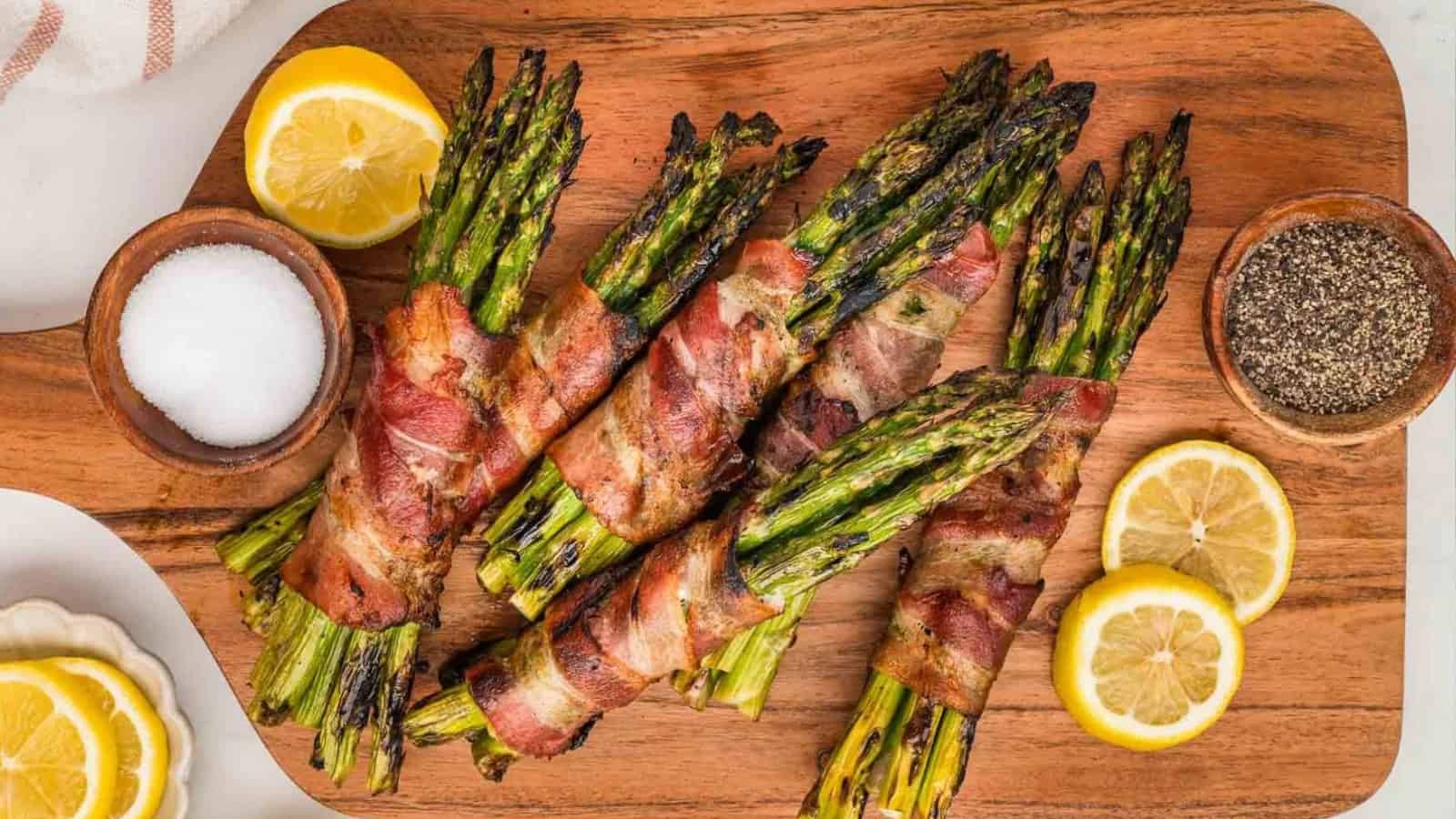 Grilled bacon-wrapped asparagus spears with crisped edges arranged on a platter.