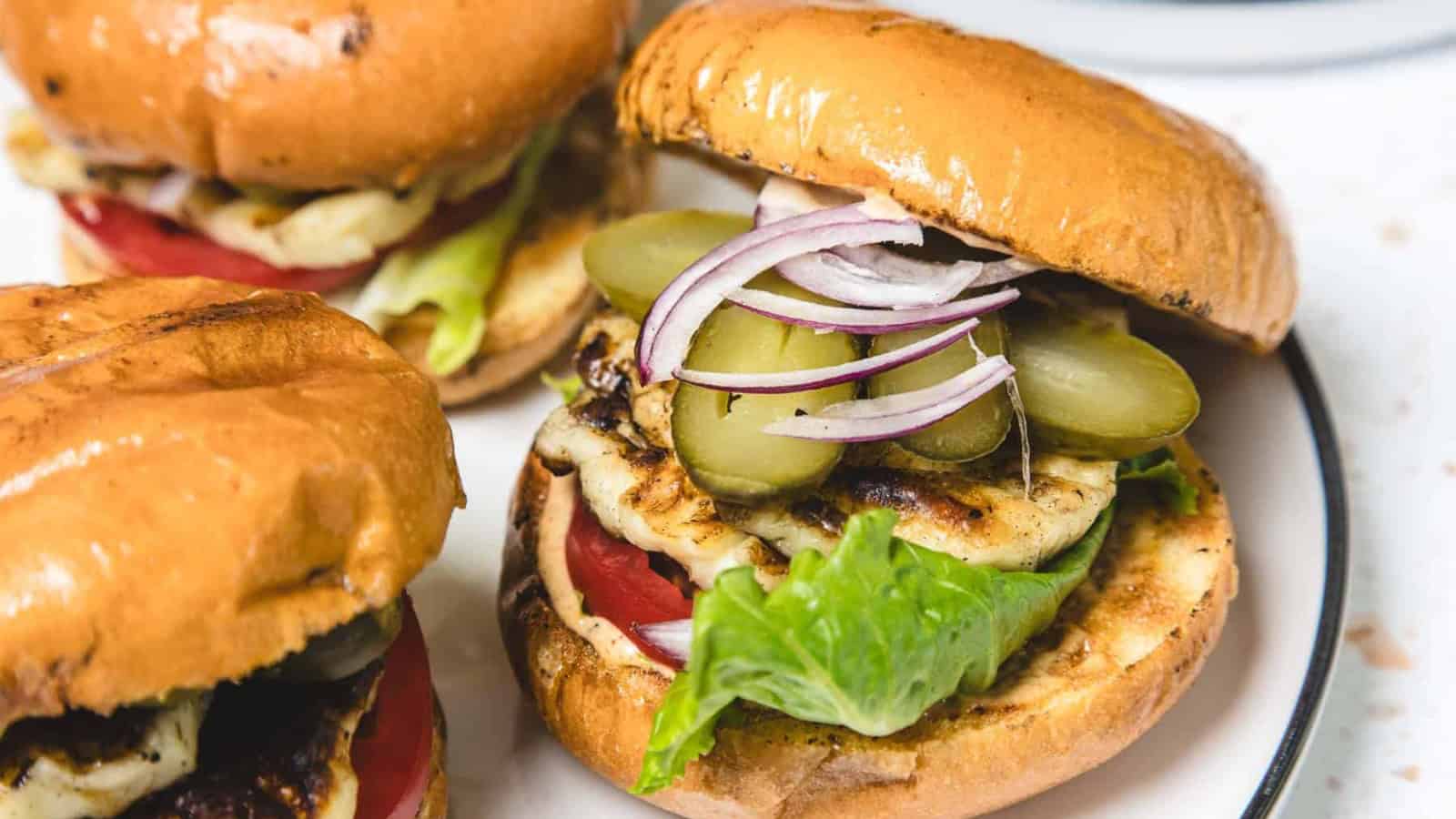 Close-up of grilled halloumi burgers with lettuce, tomato, pickles, and red onion on brioche buns.