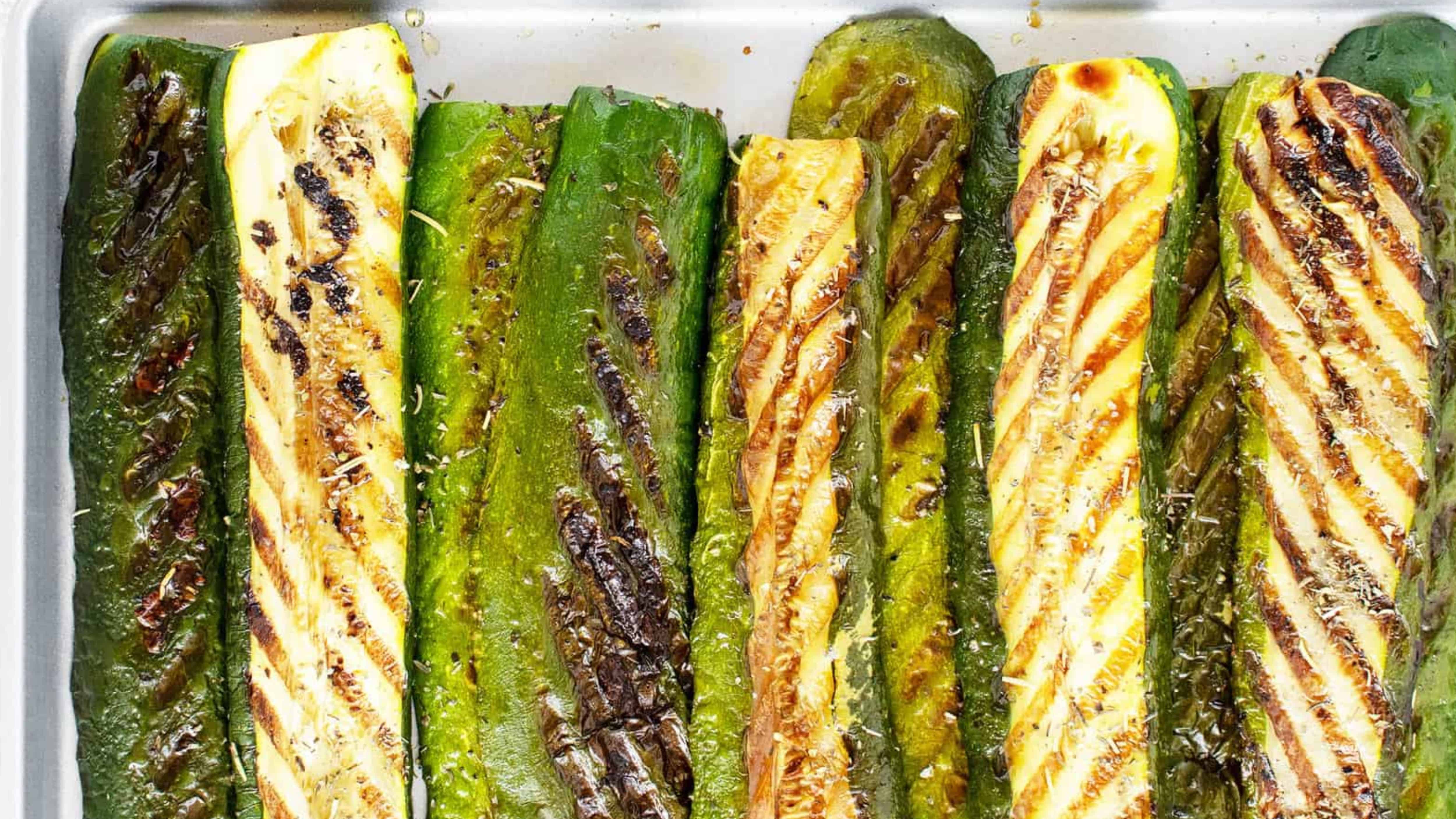 Grilled zucchini halves with charred grill marks, arranged in rows on a baking sheet.