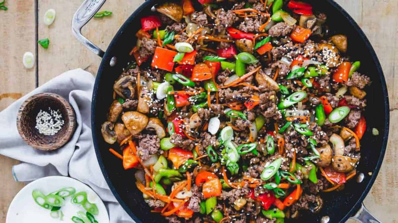 A skillet filled with stir-fried beef, colorful vegetables, and garnished with sliced green onions and sesame seeds.