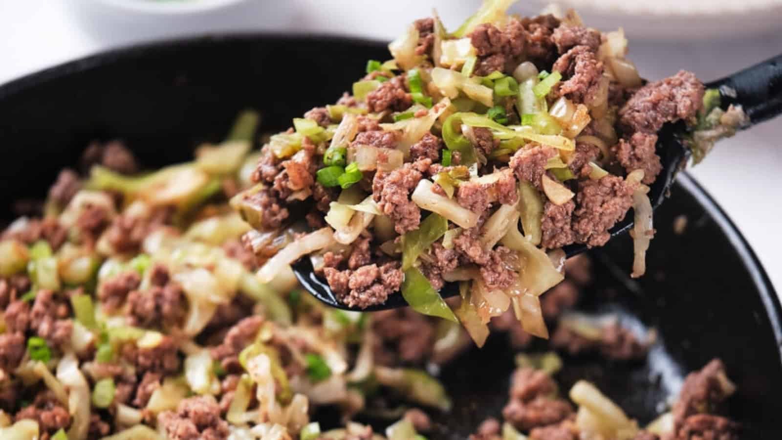 Cooked ground beef with chopped cabbage and green onions on a spoon over a skillet.