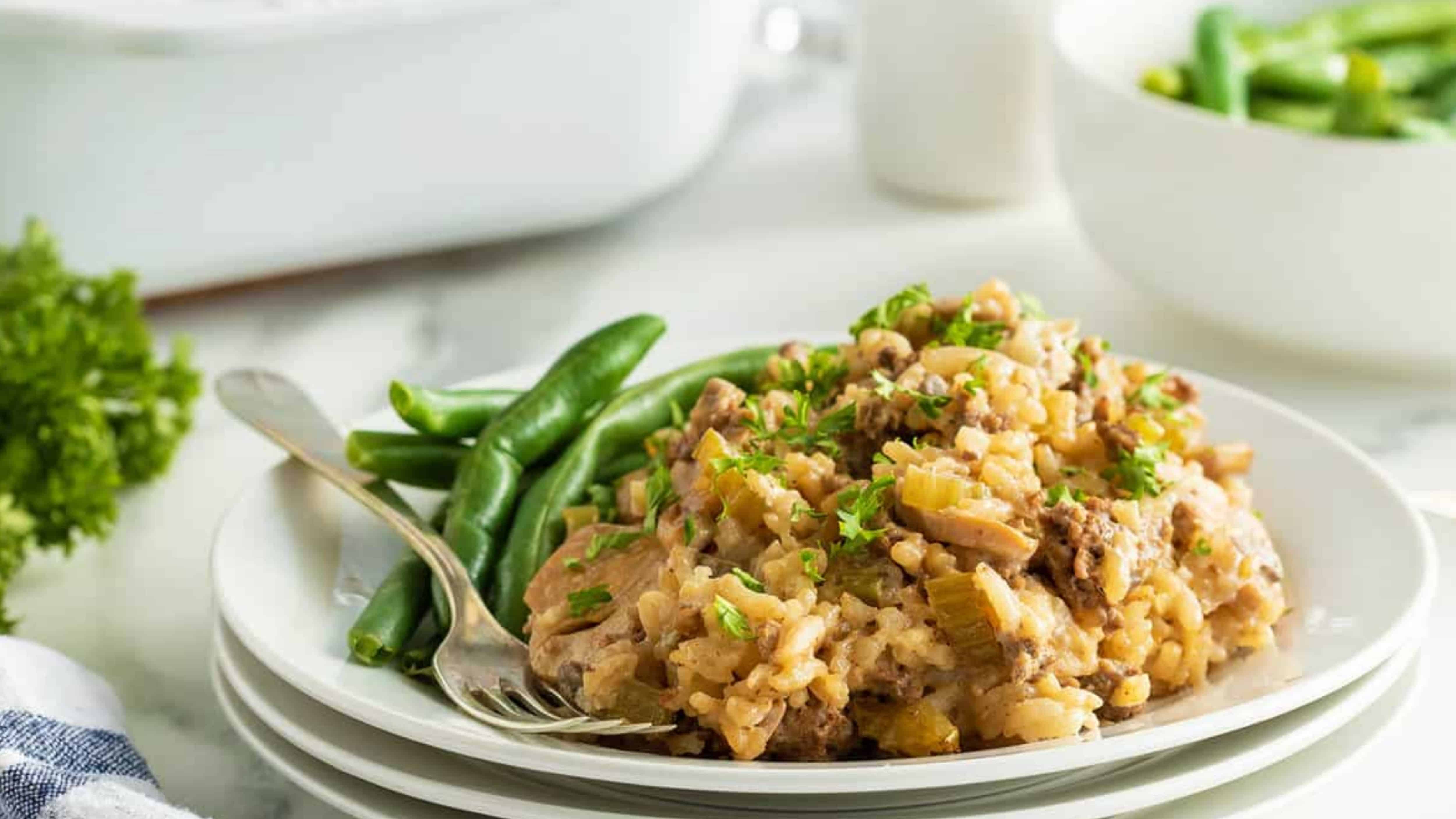 A plate of green beans and creamy rice casserole with parsley, served with a fork on a white plate.