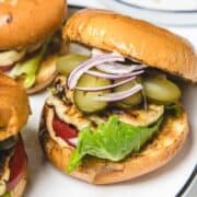 A grilled Halloumi Burger with lettuce, tomato, pickles, and red onion on a toasted bun.
