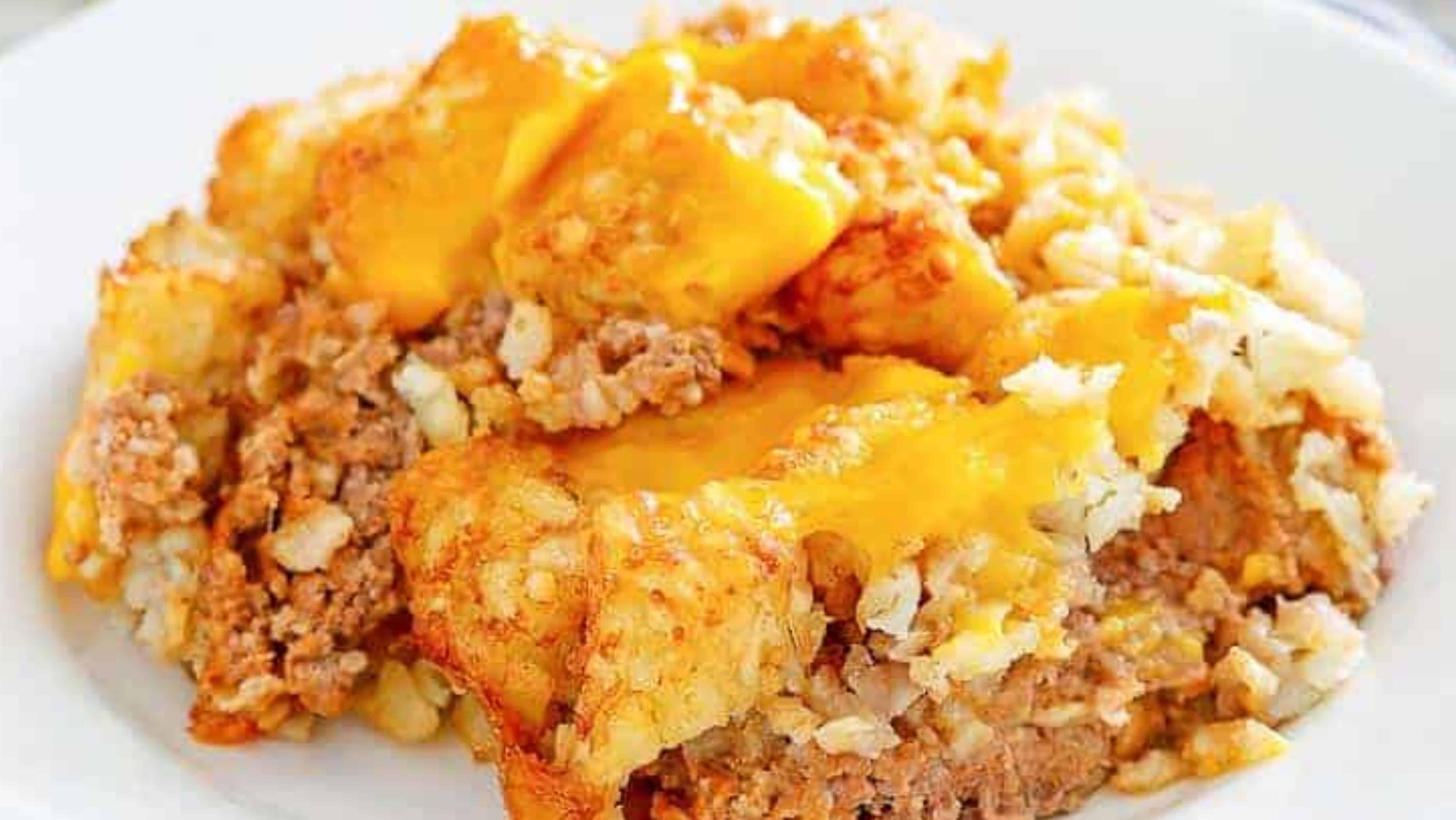 A close-up of a cheesy tater tot casserole with ground beef served on a white plate.