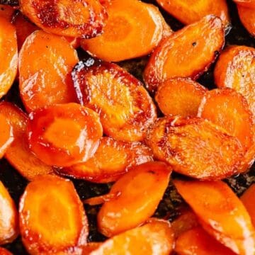 Sliced roasted carrots with a caramelized glaze on a baking sheet.