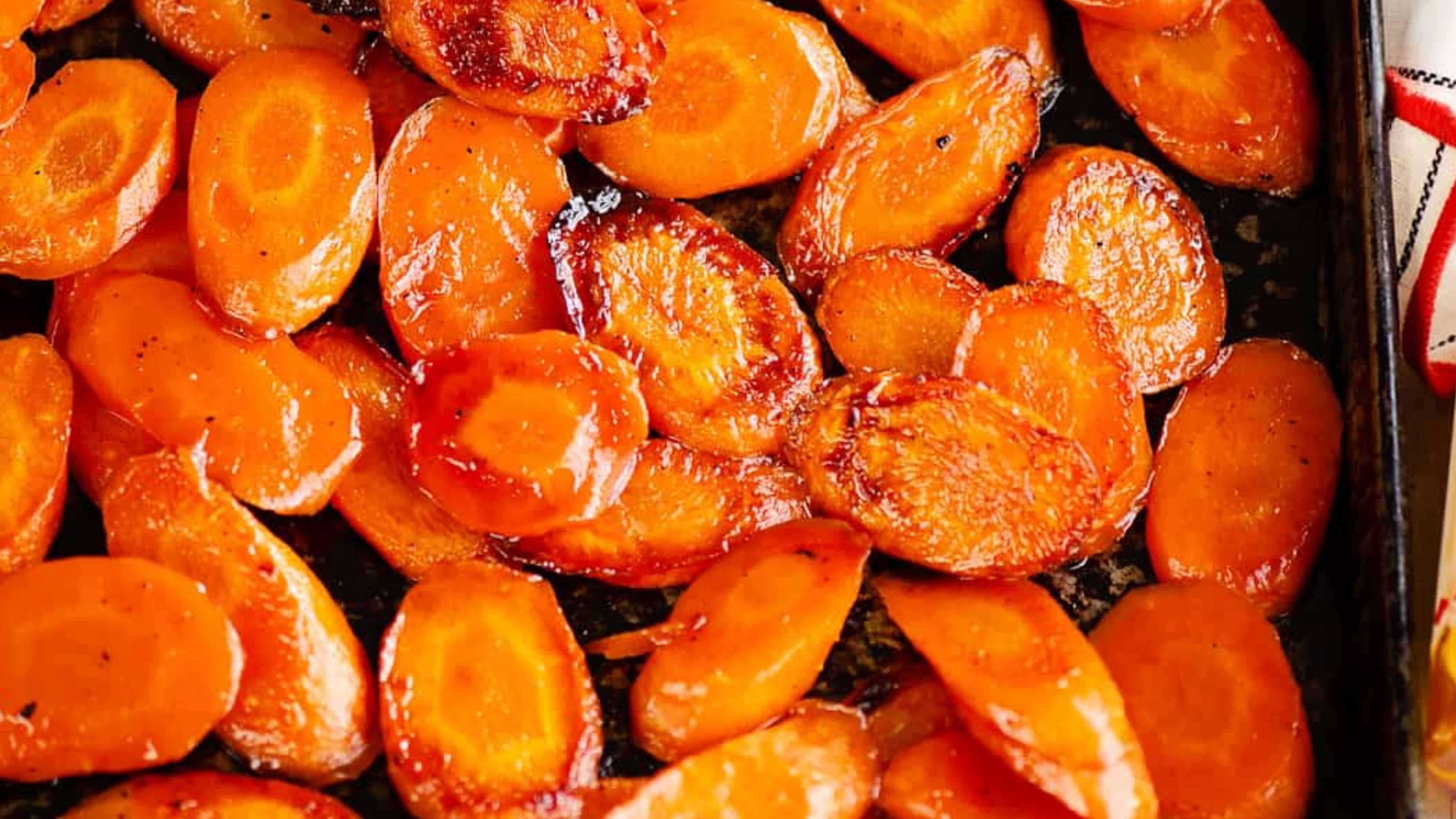 Sliced roasted carrots with a caramelized glaze on a baking sheet.