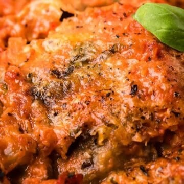 Close-up of baked lasagna with a golden cheese crust, topped with fresh basil leaves.
