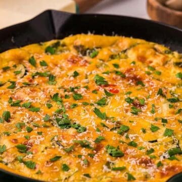 A baked frittata in a skillet, topped with melted cheese and chopped parsley.