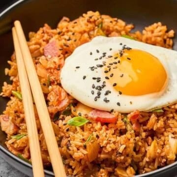 A bowl of fried rice topped with a sunny-side-up egg and black sesame seeds, with chopsticks on the side.
