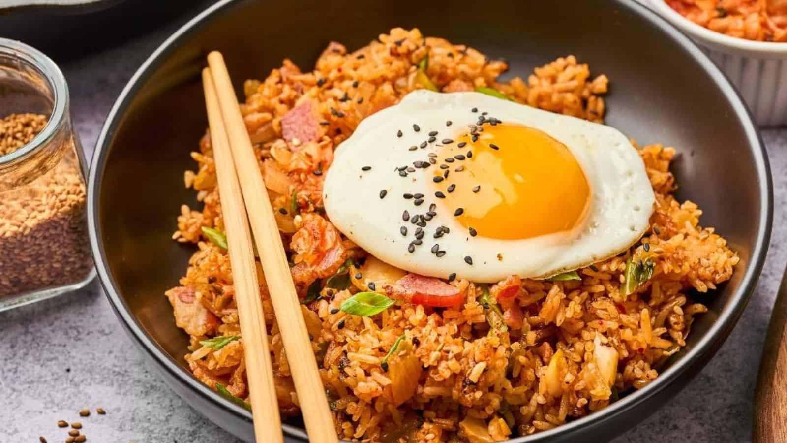 A bowl of fried rice topped with a sunny-side-up egg and black sesame seeds, with chopsticks on the side.