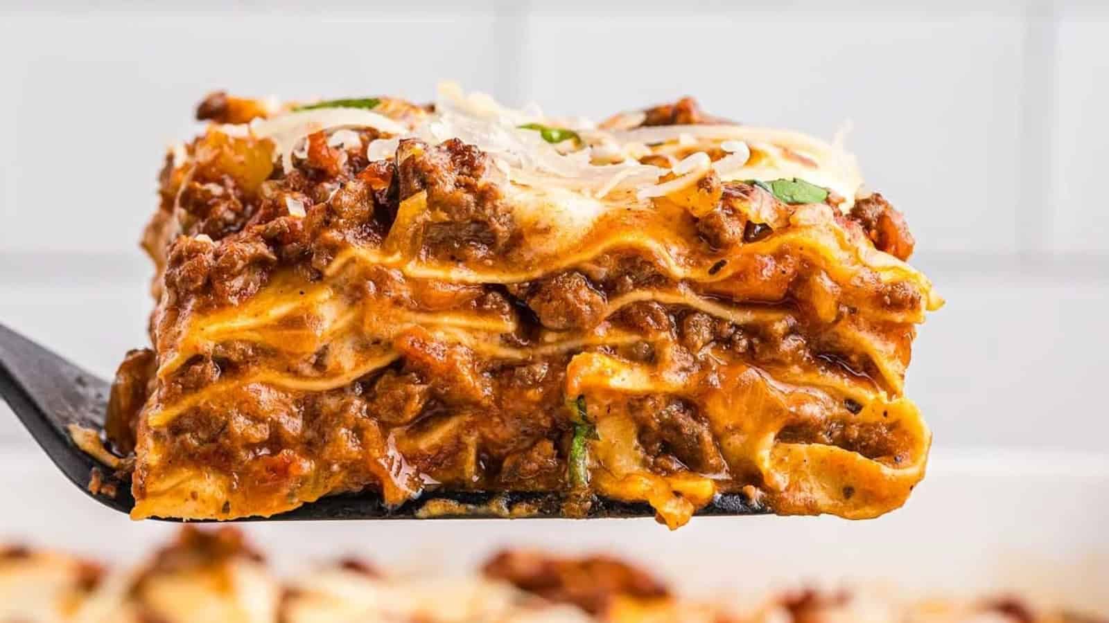 A close-up of a cheesy, meaty lasagna slice being lifted with a spatula.