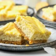 Two lemon cheesecake bars stacked on a plate, showing creamy filling and crumbly crust.