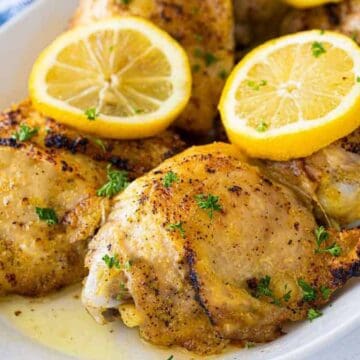 Grilled chicken thighs garnished with lemon slices and chopped parsley on a white plate.