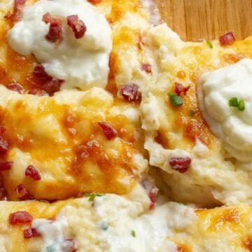 Baked mashed potatoes topped with melted cheese, bacon bits, and dollops of sour cream in a casserole dish.