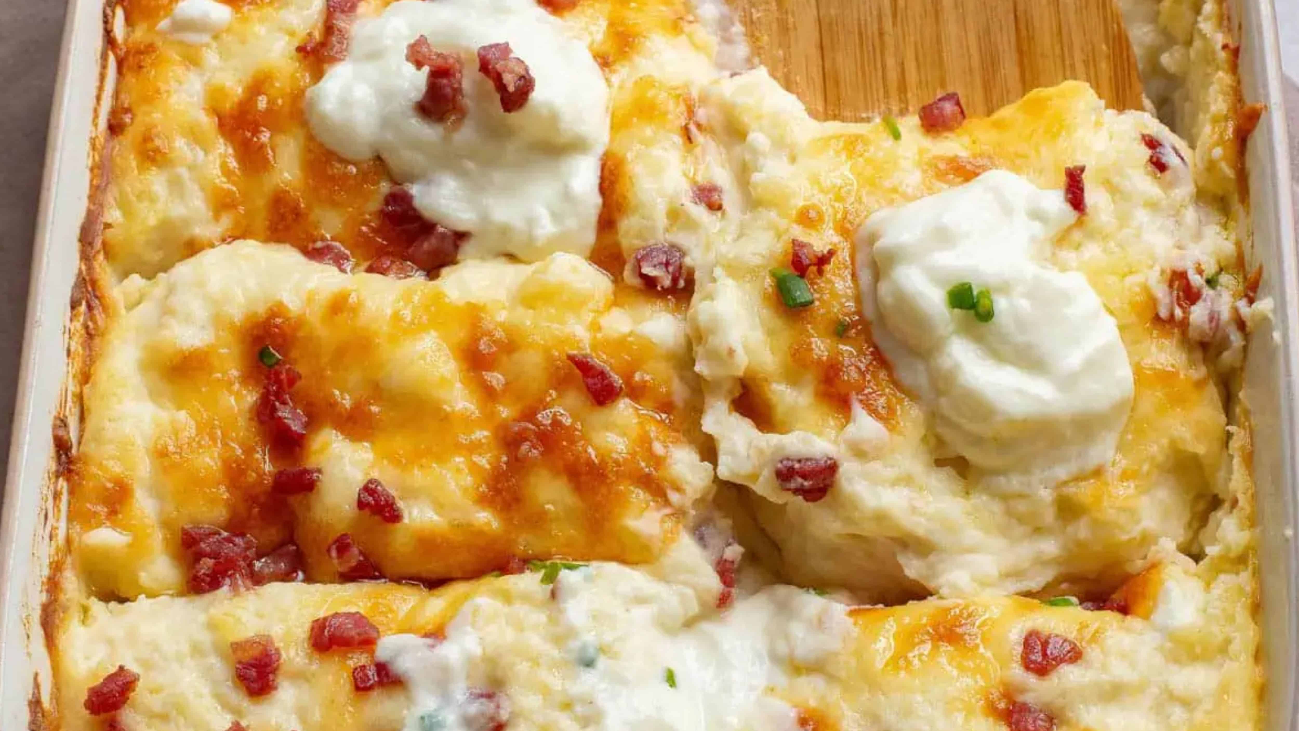 Baked mashed potatoes topped with melted cheese, bacon bits, and dollops of sour cream in a casserole dish.