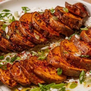 Sliced roasted sweet potatoes on a bed of creamy yogurt, garnished with green onions and spices.
