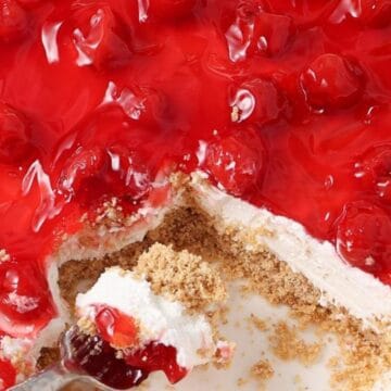 A slice of cherry cheesecake with a graham cracker crust is being served.