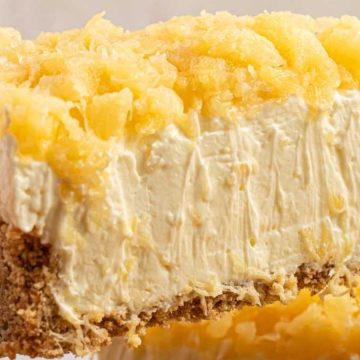 A slice of creamy pineapple cheesecake with a graham cracker crust and pineapple topping on a spatula—perfect for No-Bake Summer Desserts.