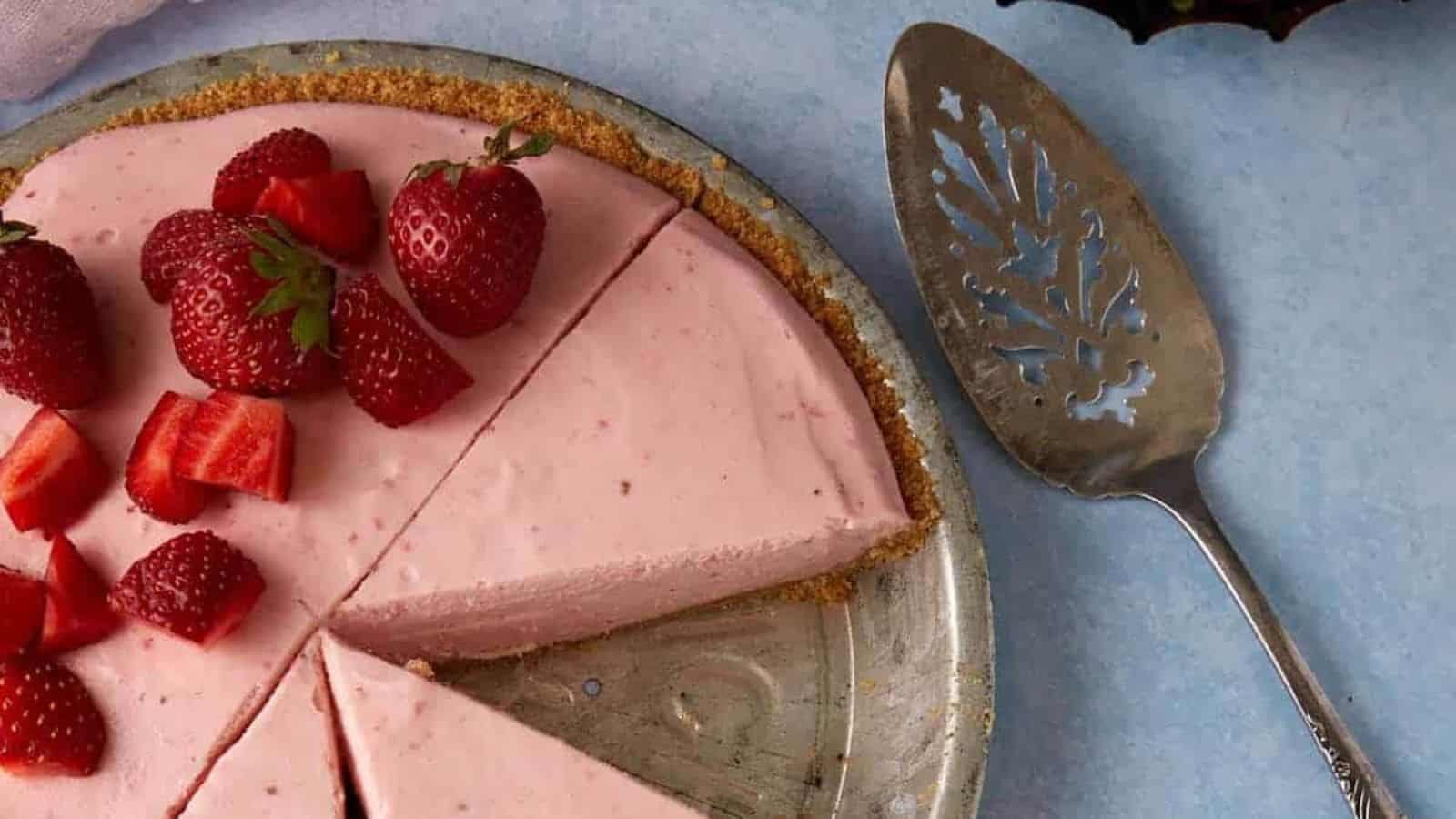 A strawberry cheesecake with sliced and whole strawberries on top, missing one slice, next to a pie server.