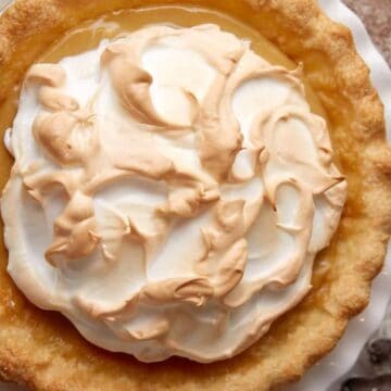 A lemon meringue pie with toasted meringue topping on a white plate, next to some forks and small plates.