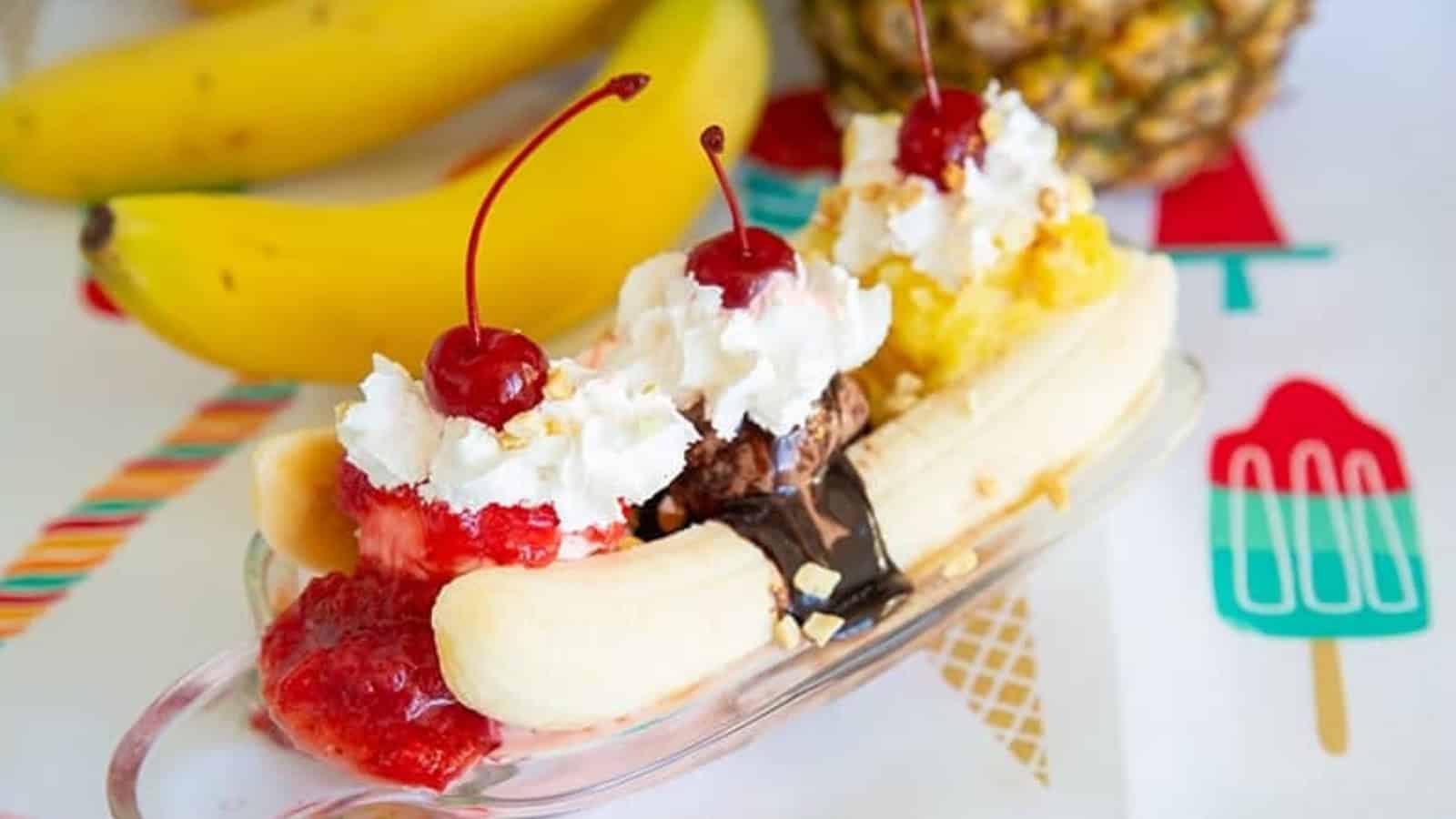 Banana split sundae with ice cream, whipped cream, cherries, and bananas on a colorful tablecloth.
