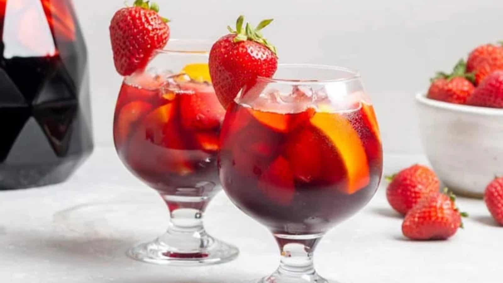 Two glasses of red sangria with ice, orange slices, and strawberries, each garnished with a whole strawberry.