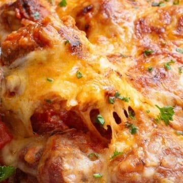 A cheesy baked meatball casserole topped with melted cheese and parsley, being served with a spoon.