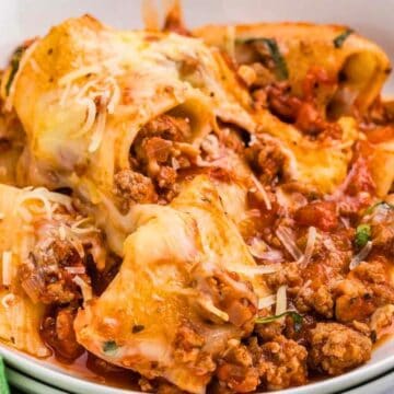 A white plate of baked pasta shells stuffed with meat and cheese, topped with marinara sauce and melted cheese.