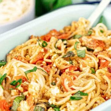 Baked spaghetti with tomatoes, crumbled cheese, and fresh basil in a white dish with a serving fork.