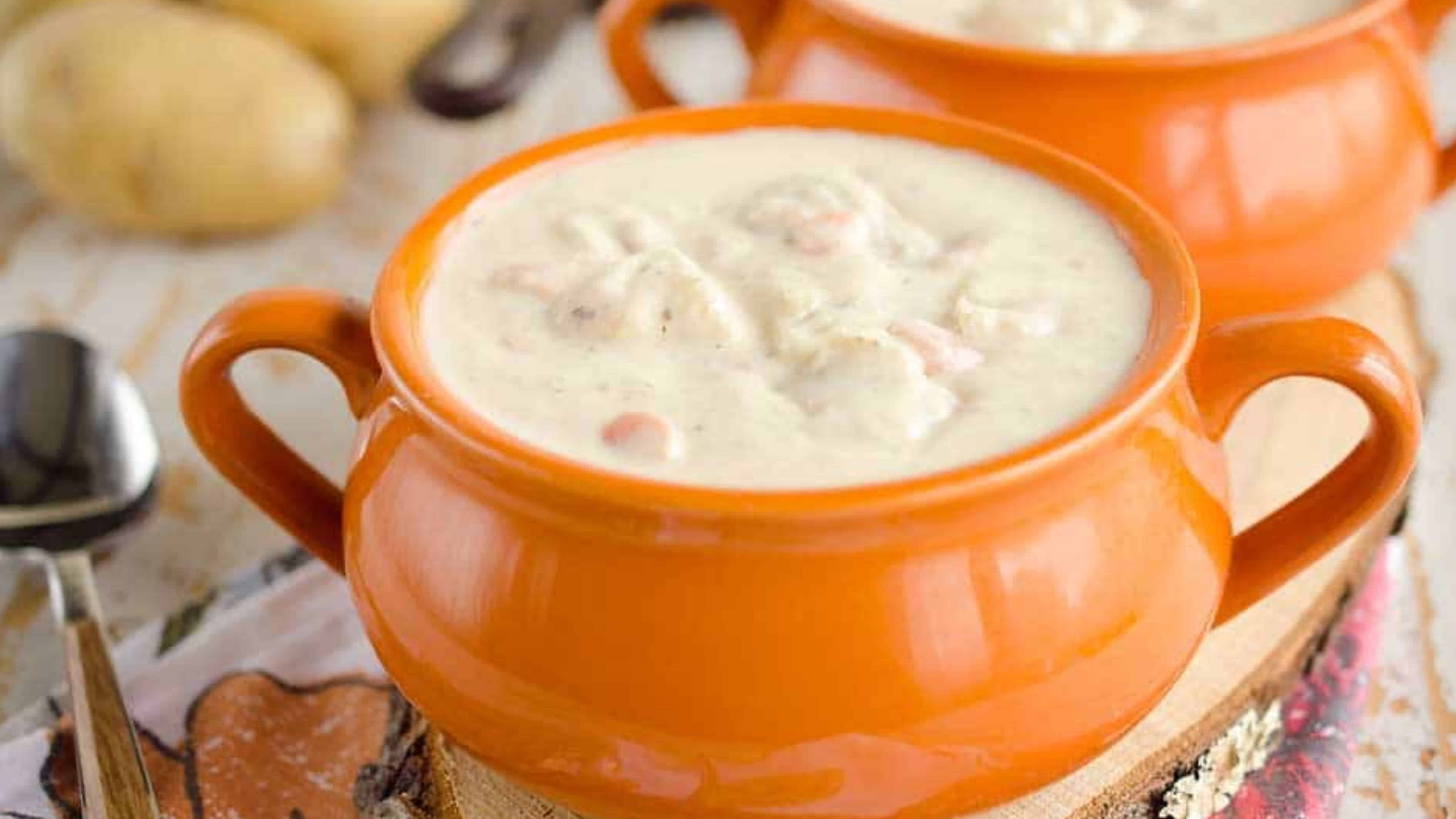 Creamy soup with chunks of vegetables served in an orange ceramic bowl on a wooden surface.