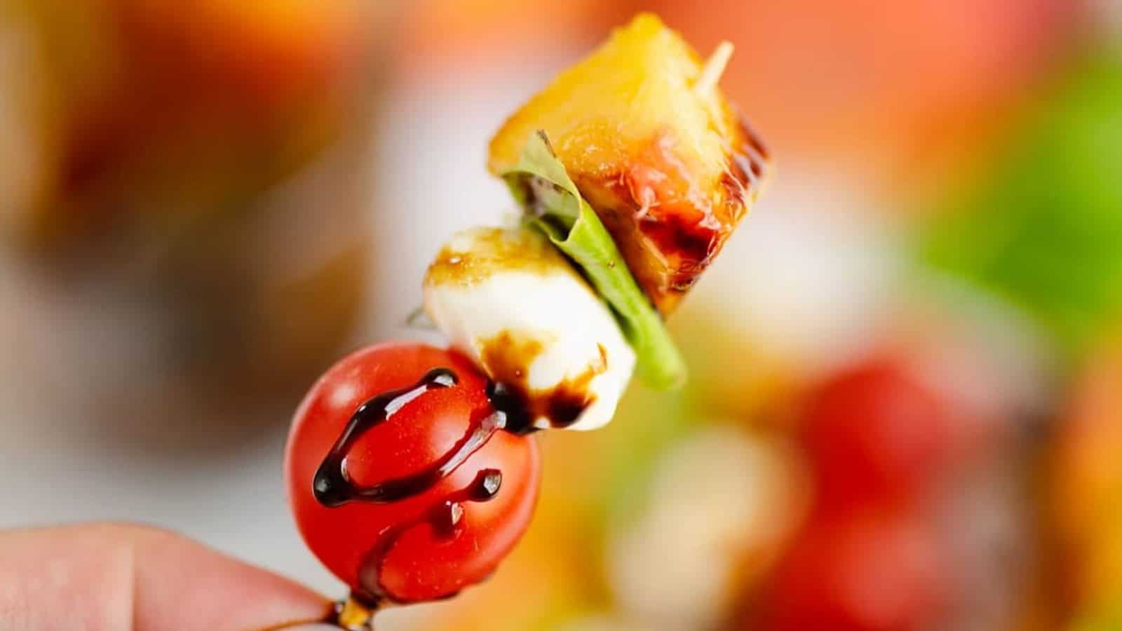 Caprese skewers with tomatoes, mozzarella, basil, and glaze on a white plate.