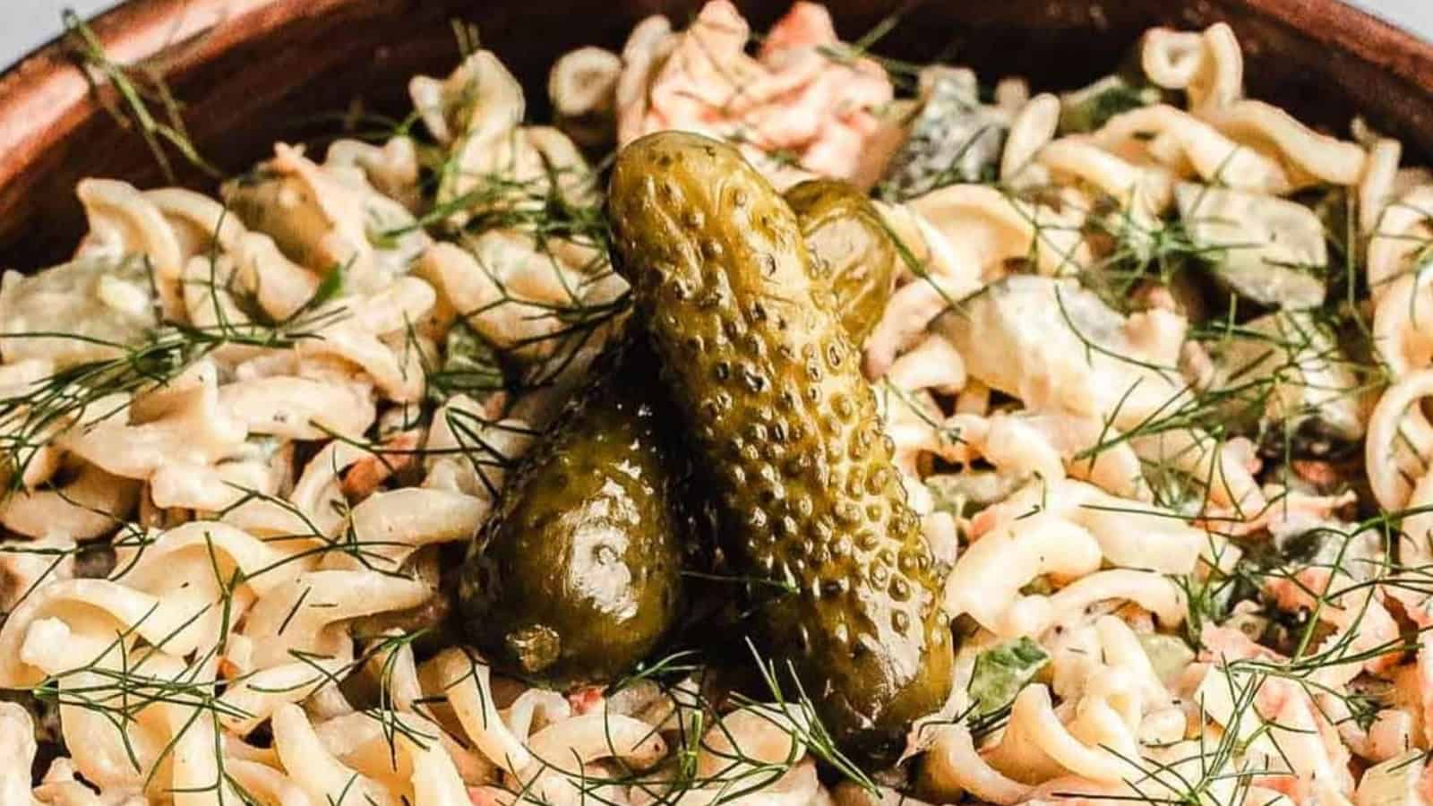 Close-up of creamy pasta salad garnished with fresh dill and topped with two whole pickles.