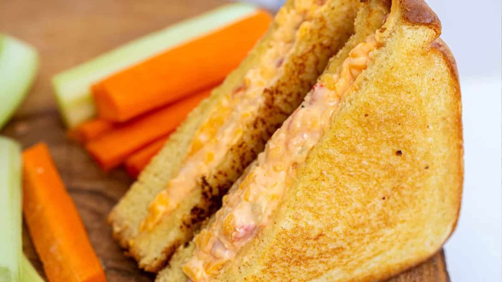 Grilled pimento cheese sandwich with carrot and celery sticks on a wooden board—a classic nod to vintage snacks.